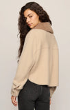 Woman wearing a beige sweater with a fur collar against a plain background